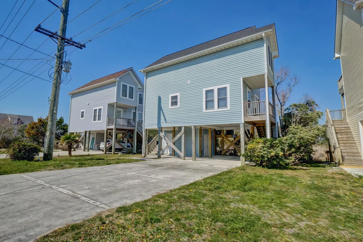 This image features the light blue exterior of the house, surrounded by lush vegetation and a driveway leading up to the home. The overall mood is cheerful, and the driveway is clearly visible, showcasing ease of access and designated parking for guests.