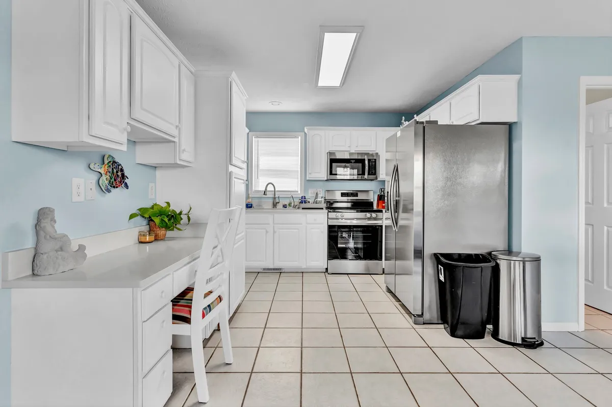 A spacious, modern kitchen with a central island offering additional seating, stainless steel appliances, white cabinetry, and tile flooring. The space is cheerful and well-lit, designed for cooking and gathering. The island seating supports casual dining or conversation while preparing meals.