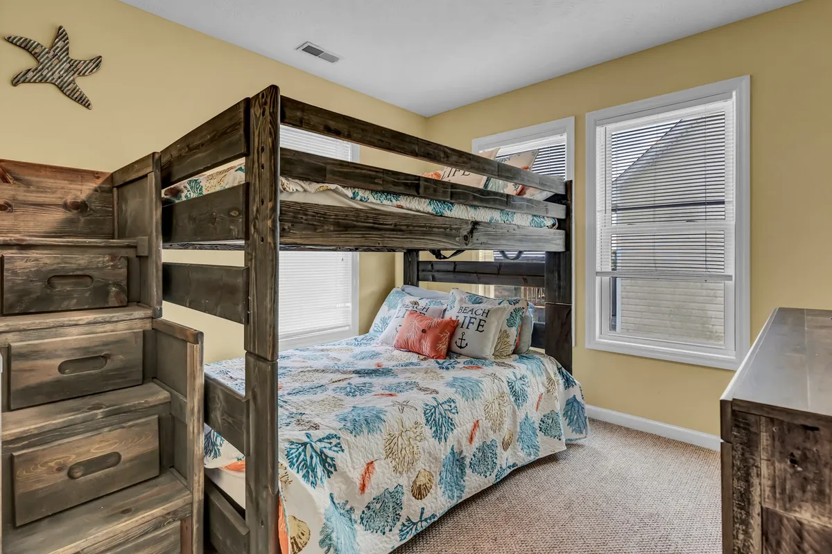 A bright, playful bedroom featuring full-sized bunk beds with colorful bedding, decorative starfish pillows, and a wooden dresser. The room radiates a fun, whimsical vibe ideal for children or the young at heart, inviting sleepovers, reading, and imaginative play.