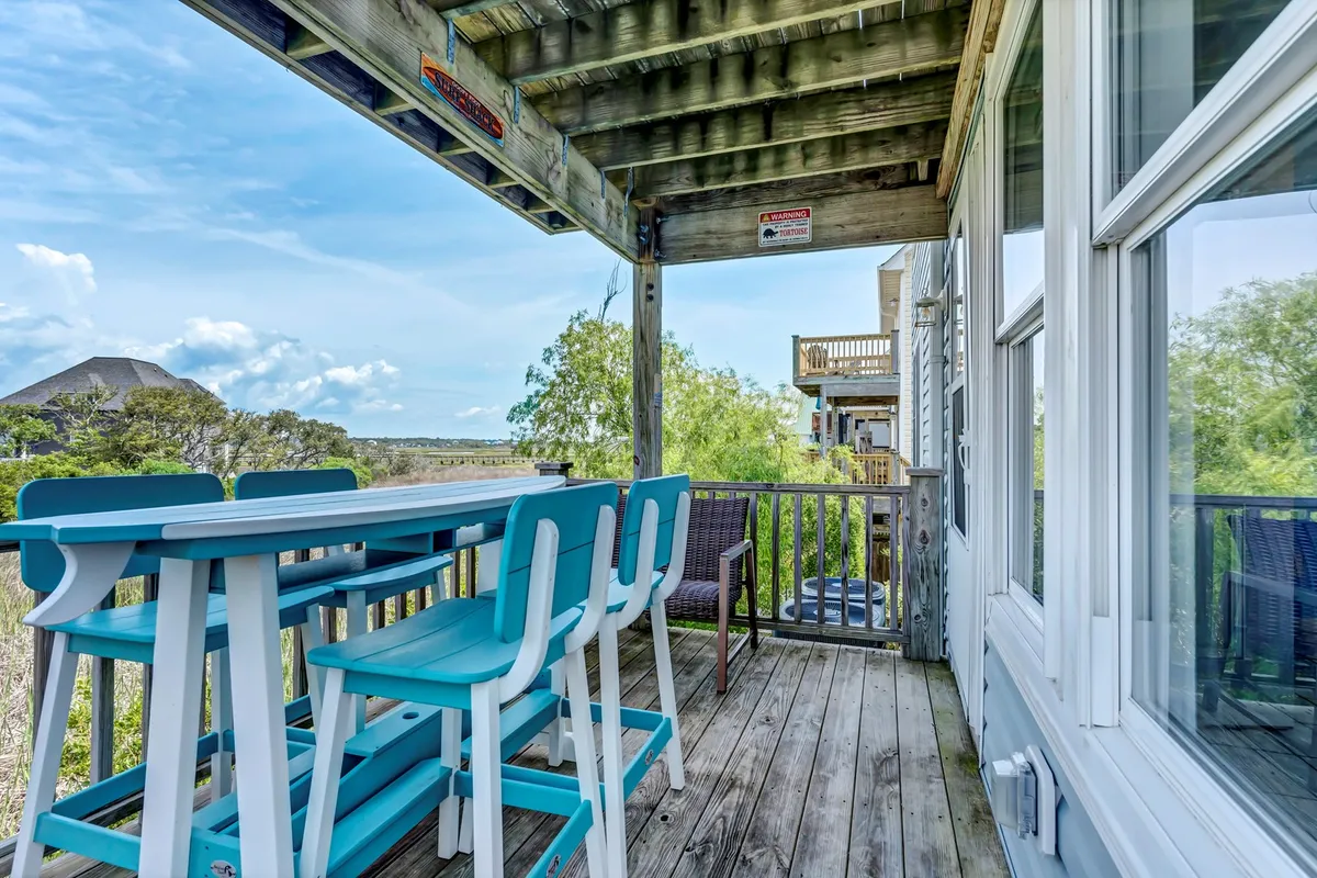 An inviting outdoor seating area on a wooden deck, complete with a sturdy railing and expansive views of the surrounding landscape and skyline. The mood is casual and welcoming, encouraging guests to relax, enjoy meals, or sip drinks as the sun sets.