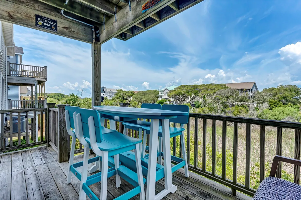 This image showcases a spacious outdoor dining table set on a private deck, surrounded by lush greenery and open sky. The inviting ambiance is perfect for morning coffee or evening gatherings, with the orientation suggesting an ideal vantage point for sunset views. Comfortable seating emphasizes relaxation and socialization.