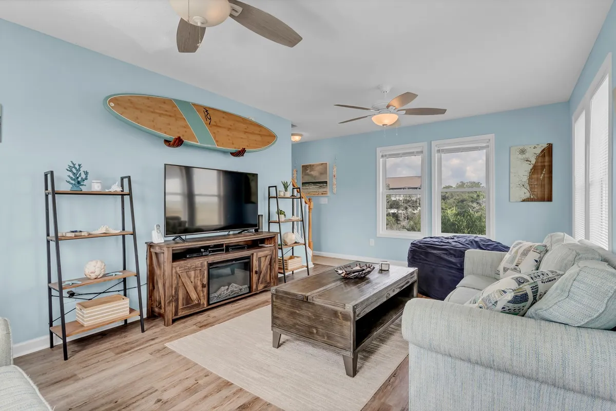 A cozy living area with a comfortable couch, a coffee table, a wall-mounted surfboard, and a television set. The space is casual yet inviting, ideal for unwinding after a workday or connecting with fellow travelers. The decor, including the surfboard, subtly references the coastal location and local activities.