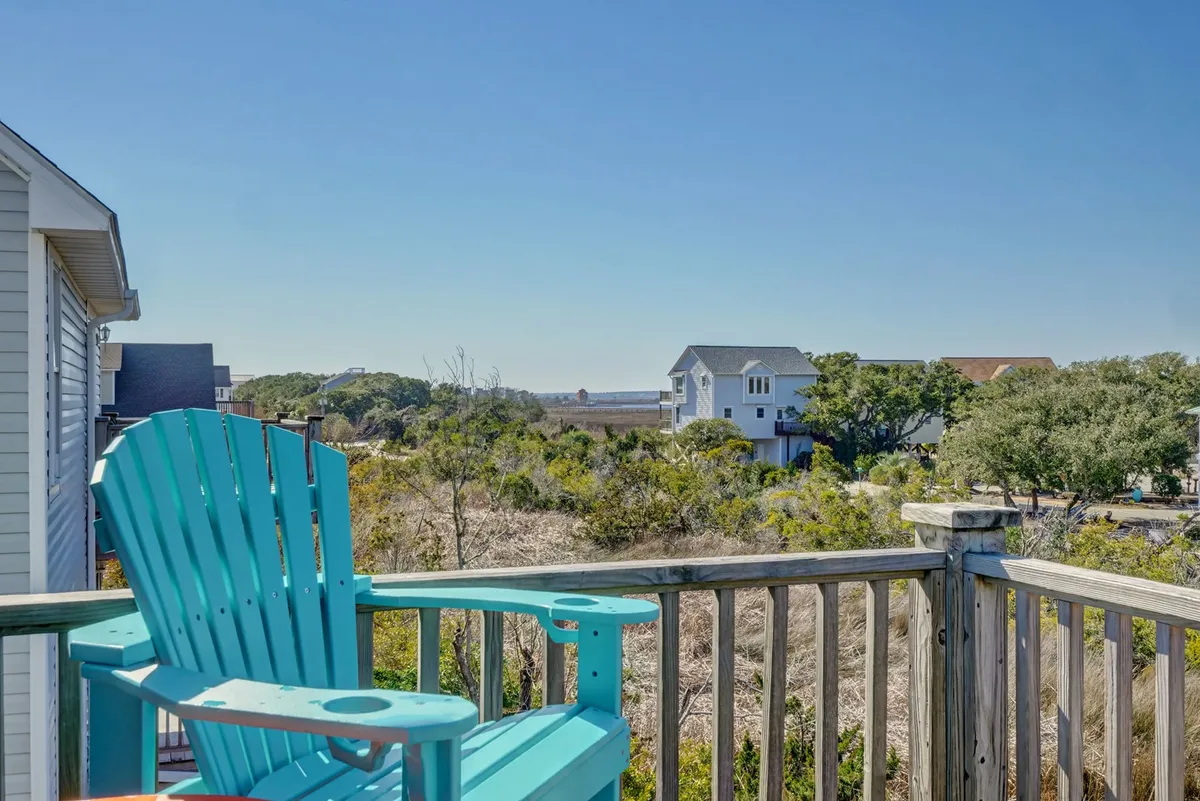 A serene turquoise Adirondack chair is positioned to overlook distant houses and natural landscape, setting the stage for peaceful moments of solitude or intimate conversation. The scene captures the tranquil beauty and potential for watching sunsets or enjoying the coastal breeze.